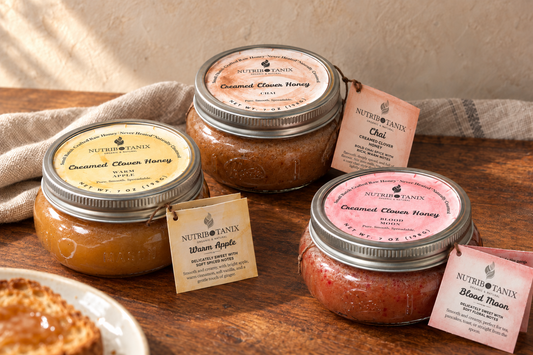 Styled composite of NutriBotanix Warm Apple, Chai, and Blood Moon Creamed Clover Honey jars on a wooden table with linen.