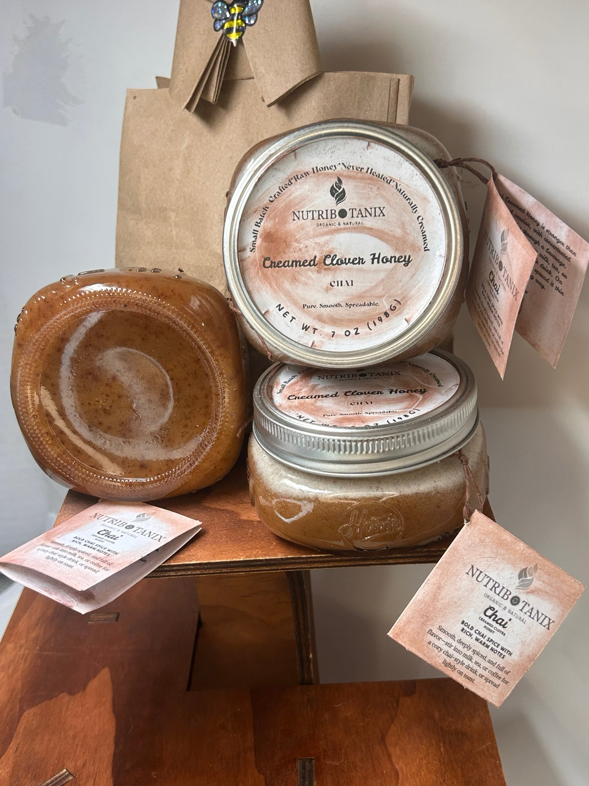 NutriBotanix Chai Creamed Clover Honey jars with labeled silver lids and paper tags on a wooden display.